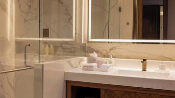 Un baño moderno con tocador de mármol, cabina de ducha de vidrio y mueble de madera.