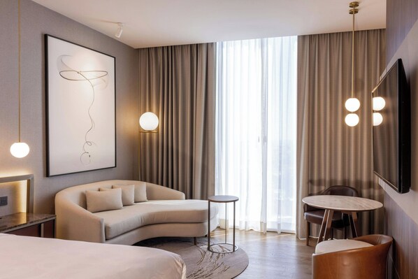 Una habitación de hotel moderna con un sofá curvo, una mesa redonda y una cama grande.