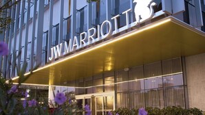 Entrada de un hotel JW Marriott con un cartel llamativo, rodeada de flores moradas.