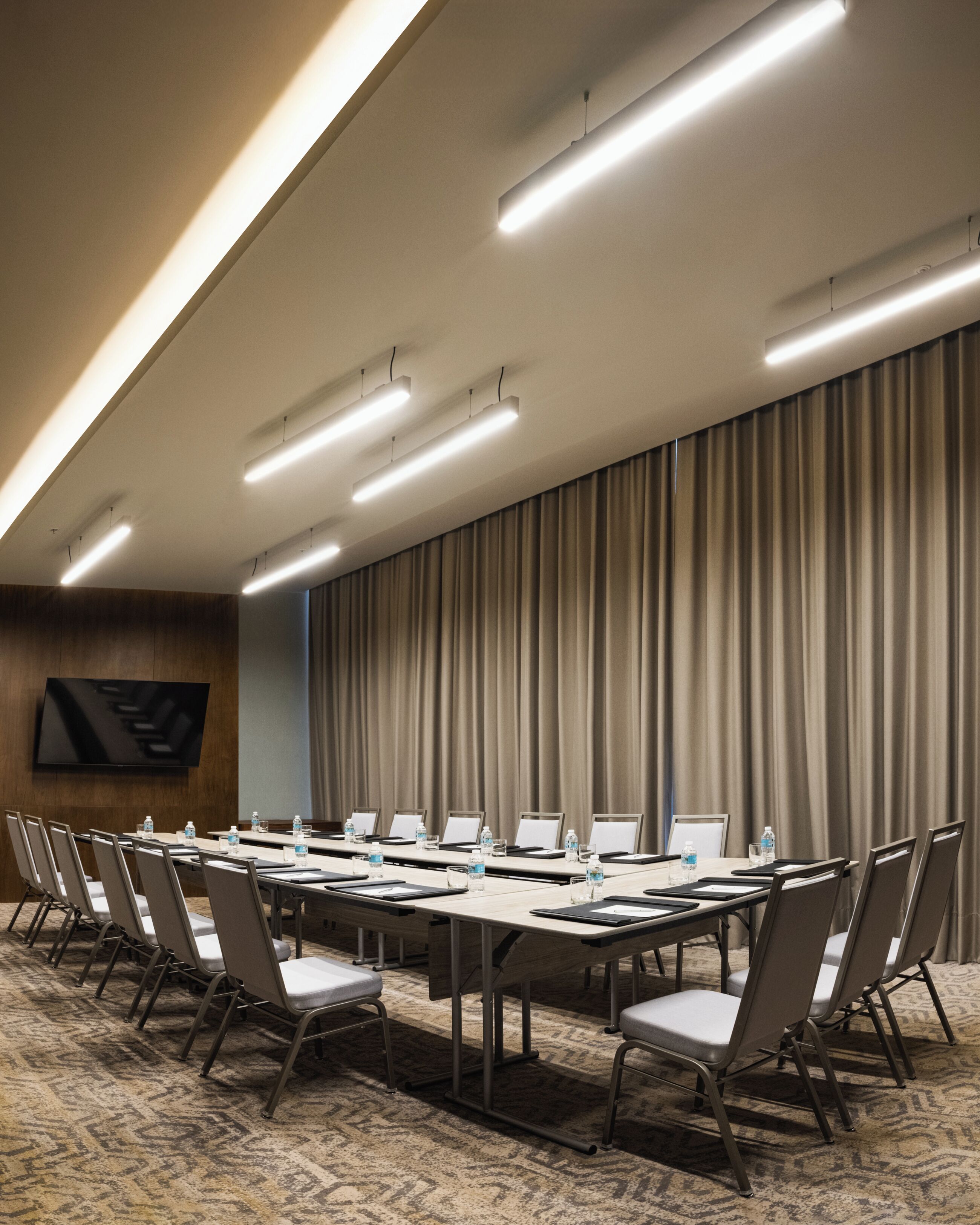 Un salón de conferencias con una mesa larga, sillas, un televisor de pantalla plana y un gran telón de fondo.