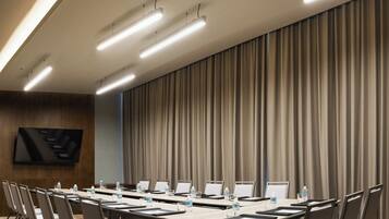 Un salón de conferencias con una mesa larga, sillas, un televisor de pantalla plana y un gran telón de fondo.