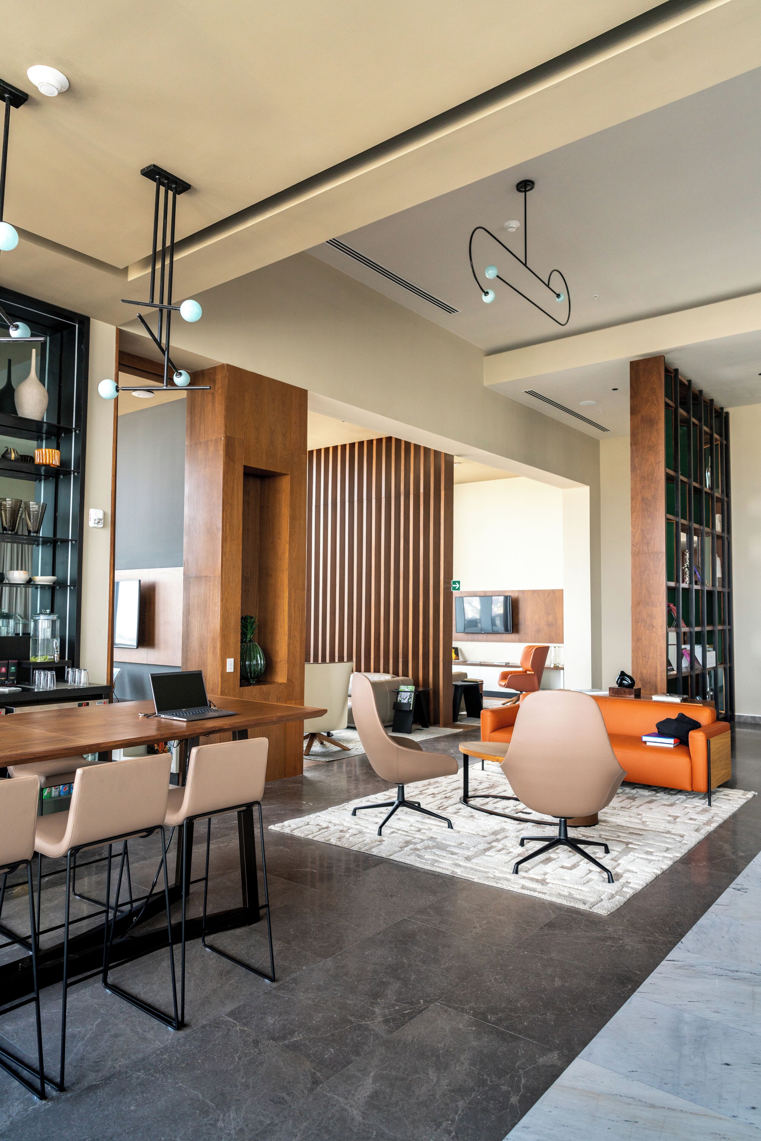 Un interior moderno con una mesa de comedor de madera, taburetes de bar, un sofá y una estantería.