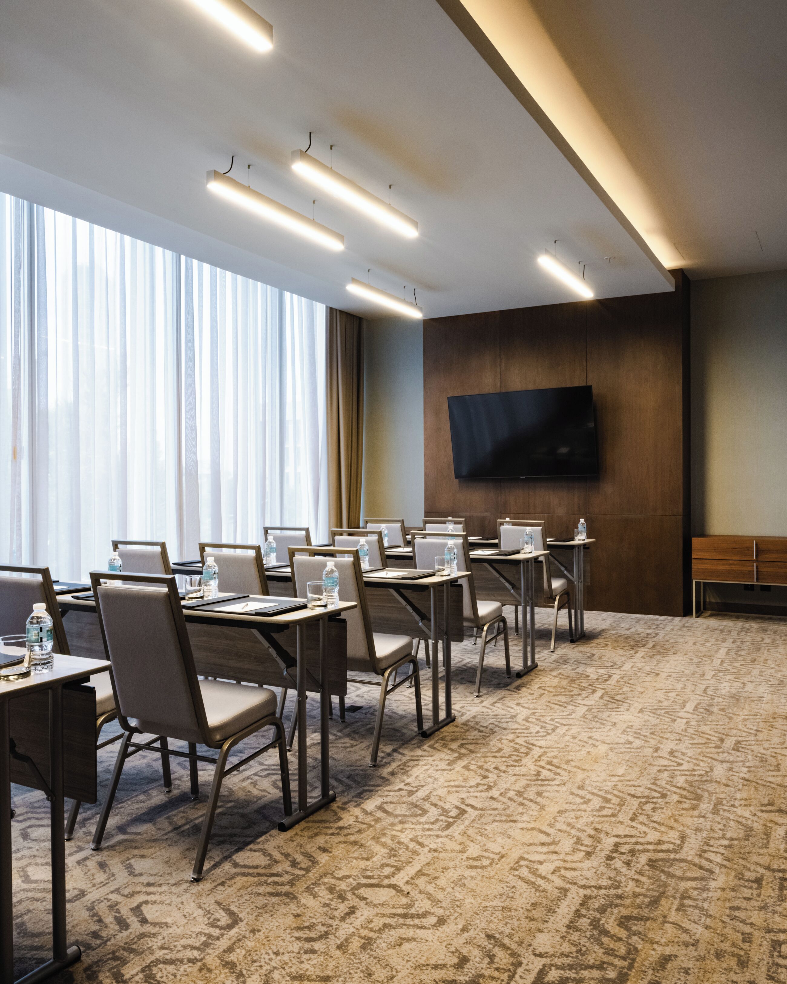 A conference room with tables, chairs, a flat-screen TV, and a large window with curtains.