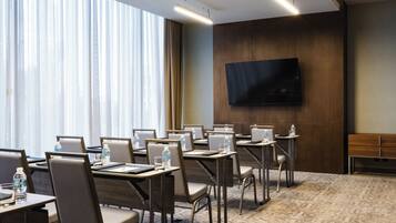 A conference room with tables, chairs, a flat-screen TV, and a large window with curtains.