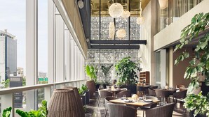 Un moderno salón en la azotea con mobiliario de mimbre, lámparas colgantes de mimbre y amplias ventanas con vistas a la ciudad.