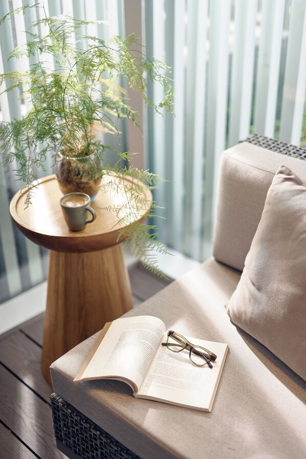 A cozy reading nook with a cushioned bench, a wooden side table with a potted plant, and an open book with glasses on it.