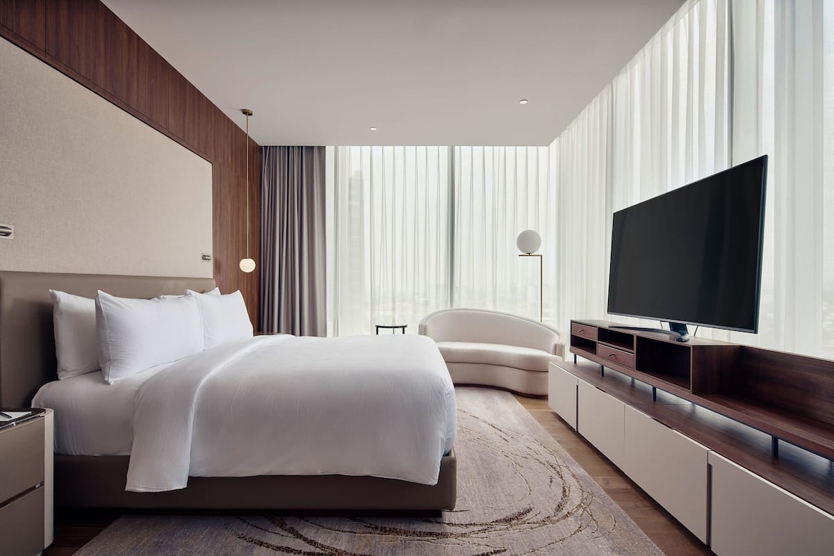 Een moderne hotelkamer met een groot bed, een flatscreen televisie, een bank en een groot raam met gordijnen.