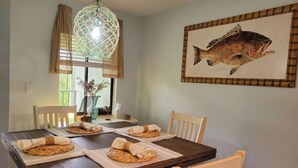 Un comedor con una mesa de madera, sillas blancas, un lámpara colgante y un cuadro de un pez enmarcado en la pared.