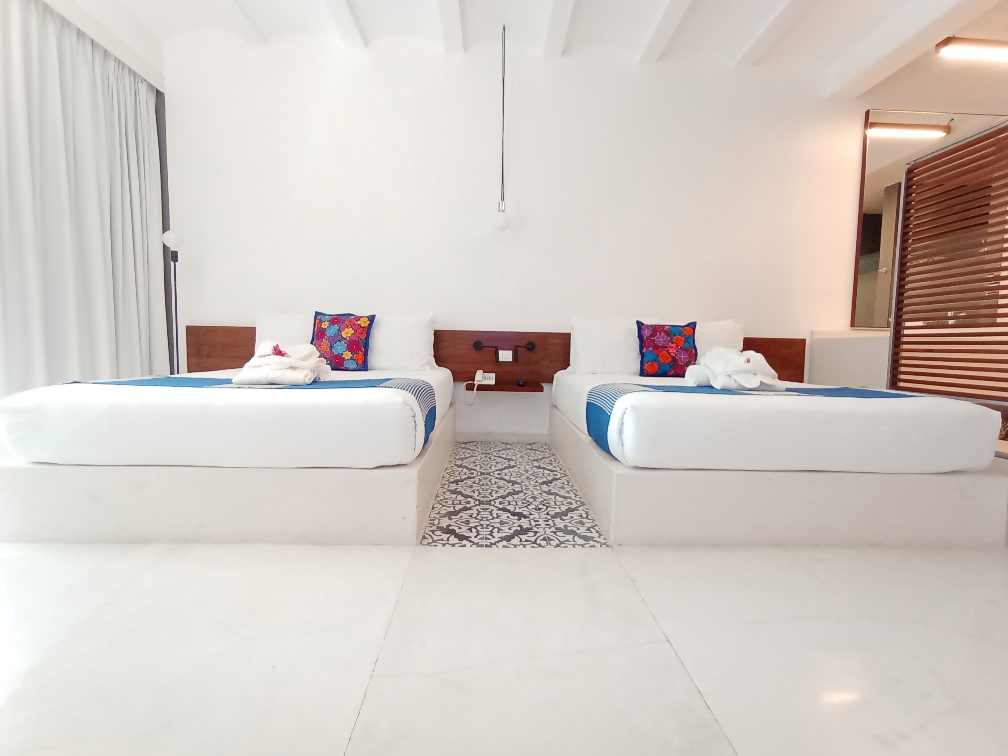 A modern hotel room with two beds, a patterned rug, a wooden headboard, and a large mirror.