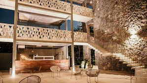 A multi-level outdoor area with a wooden reception desk, several chairs, and a staircase leading to an upper level. - Huayacán Cuernavaca Curamoria Collection (Jiutepec)