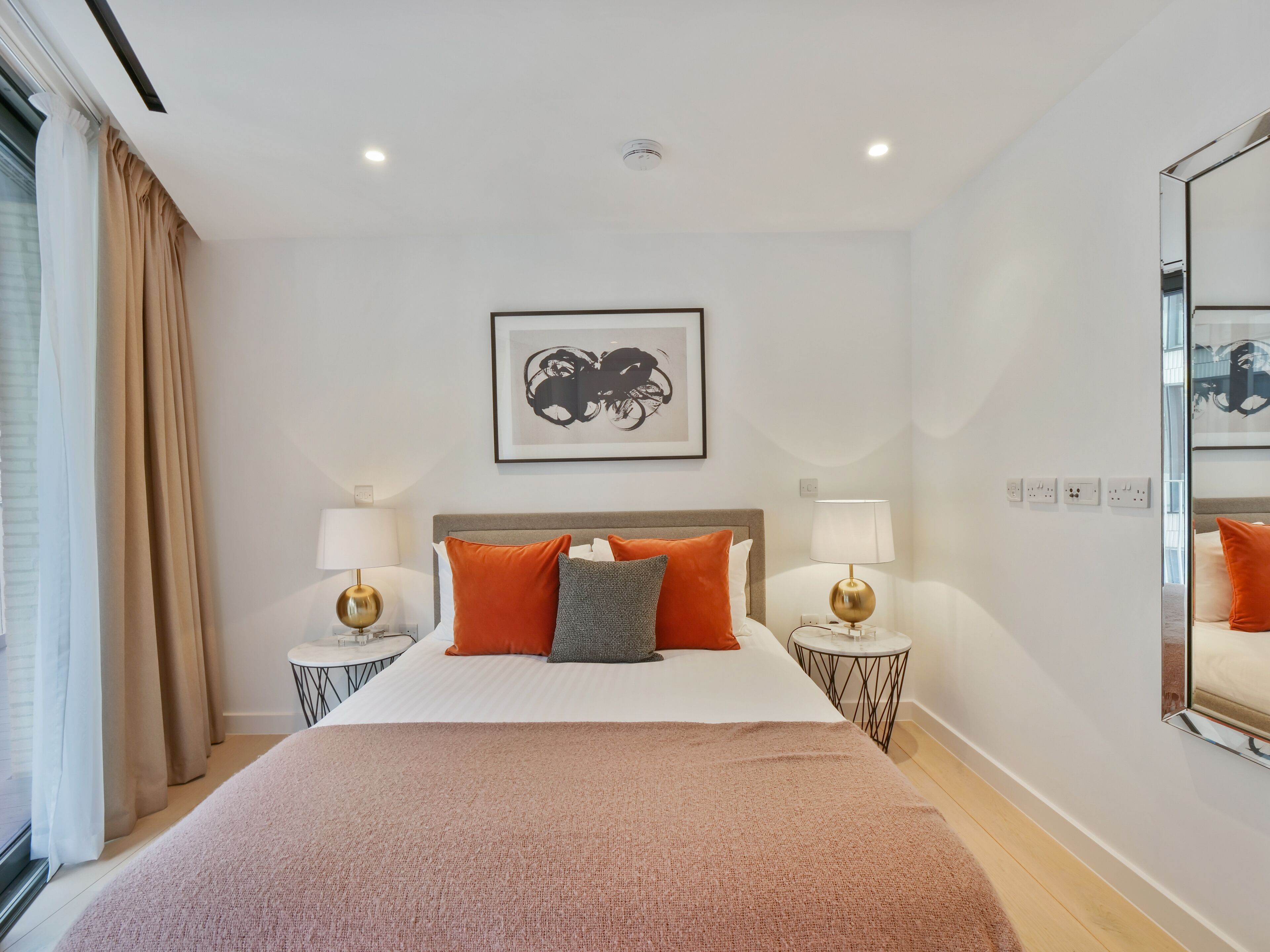 A hotel room with a large bed, two bedside tables with lamps, a framed artwork above the bed, and a mirror on the wall.