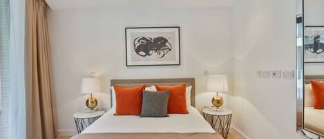 A hotel room with a large bed, two bedside tables with lamps, a framed artwork above the bed, and a mirror on the wall.