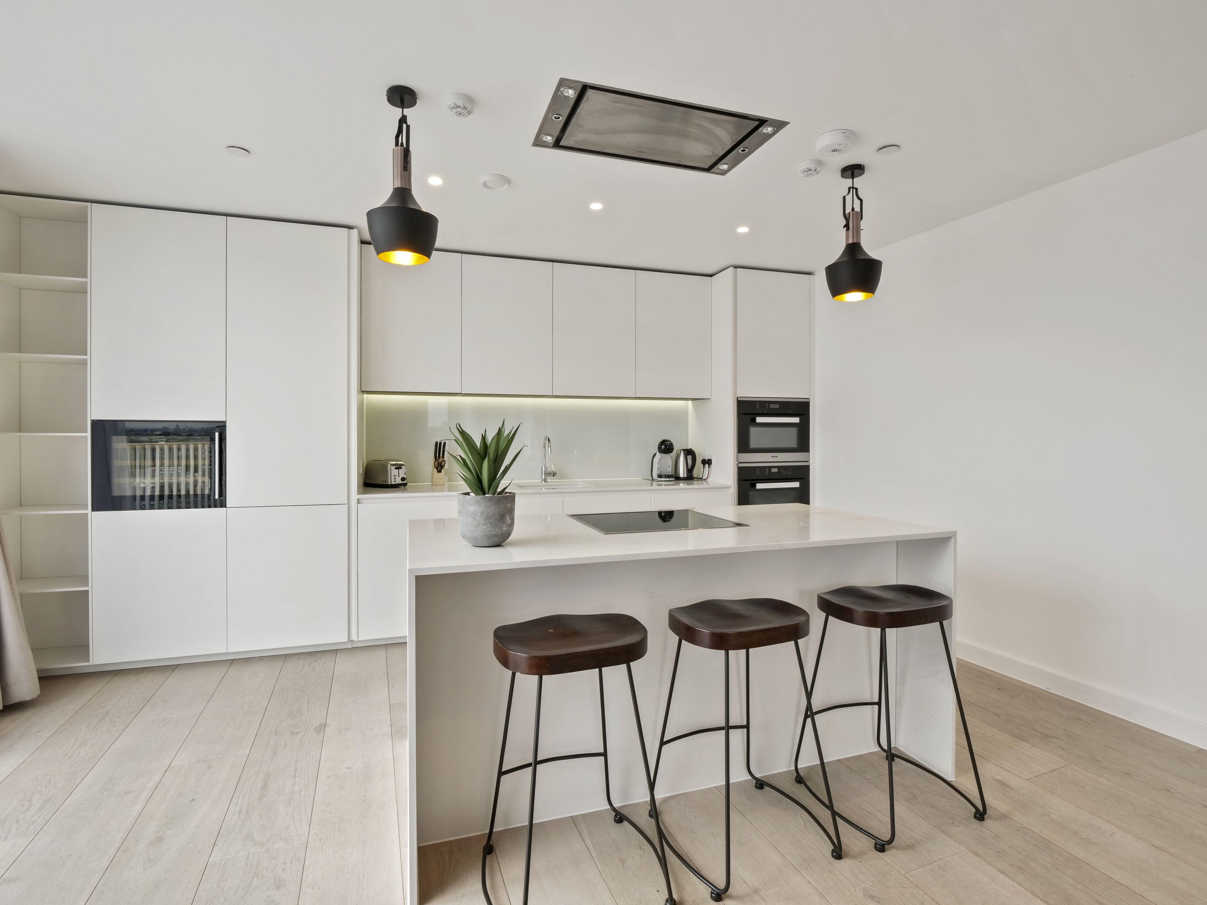 Une cuisine moderne avec des meubles blancs, un îlot central doté de tabourets et un éclairage suspendu.