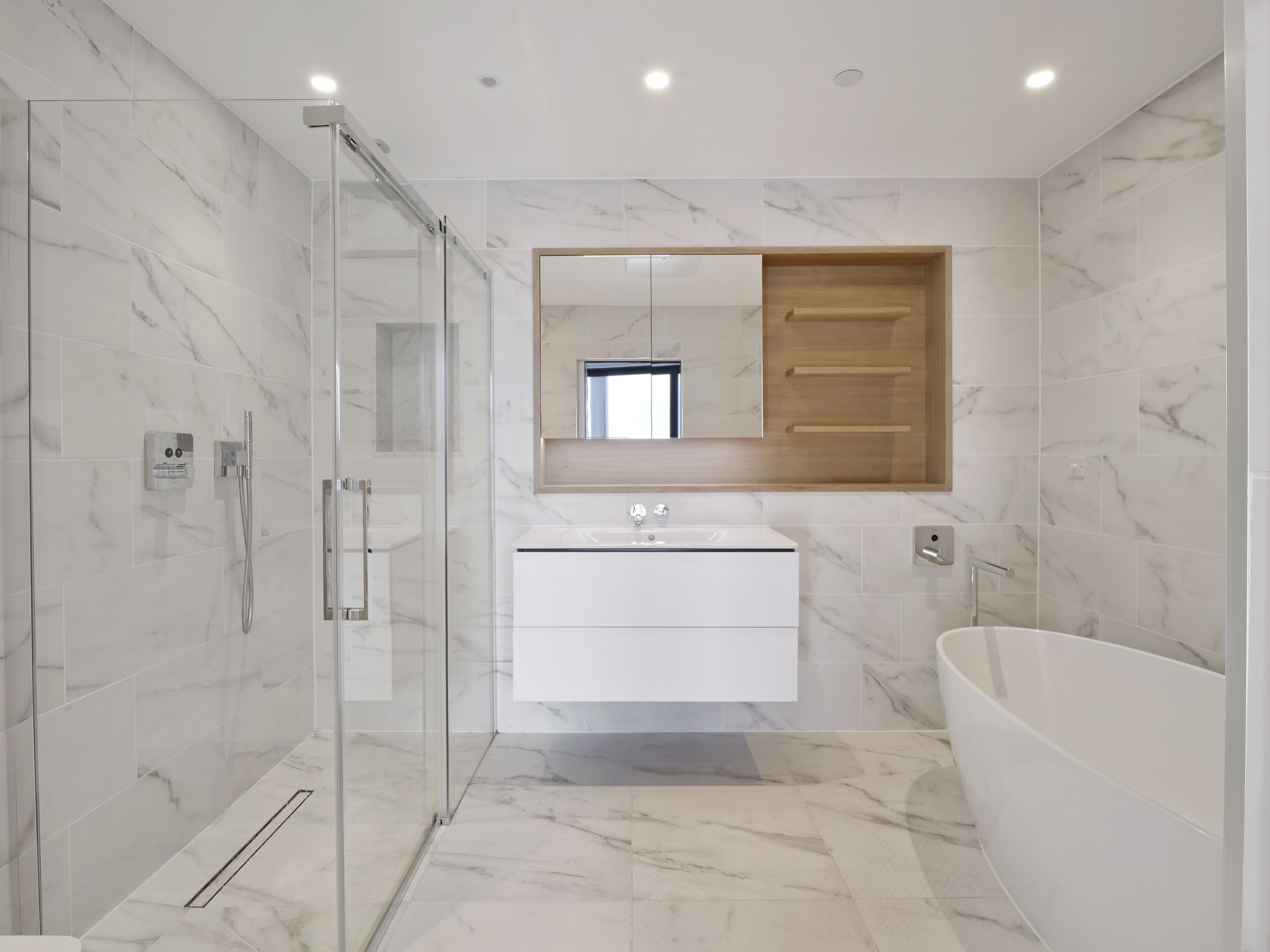 A modern bathroom with a glass-enclosed shower, a white vanity with a mirror, and a freestanding bathtub.