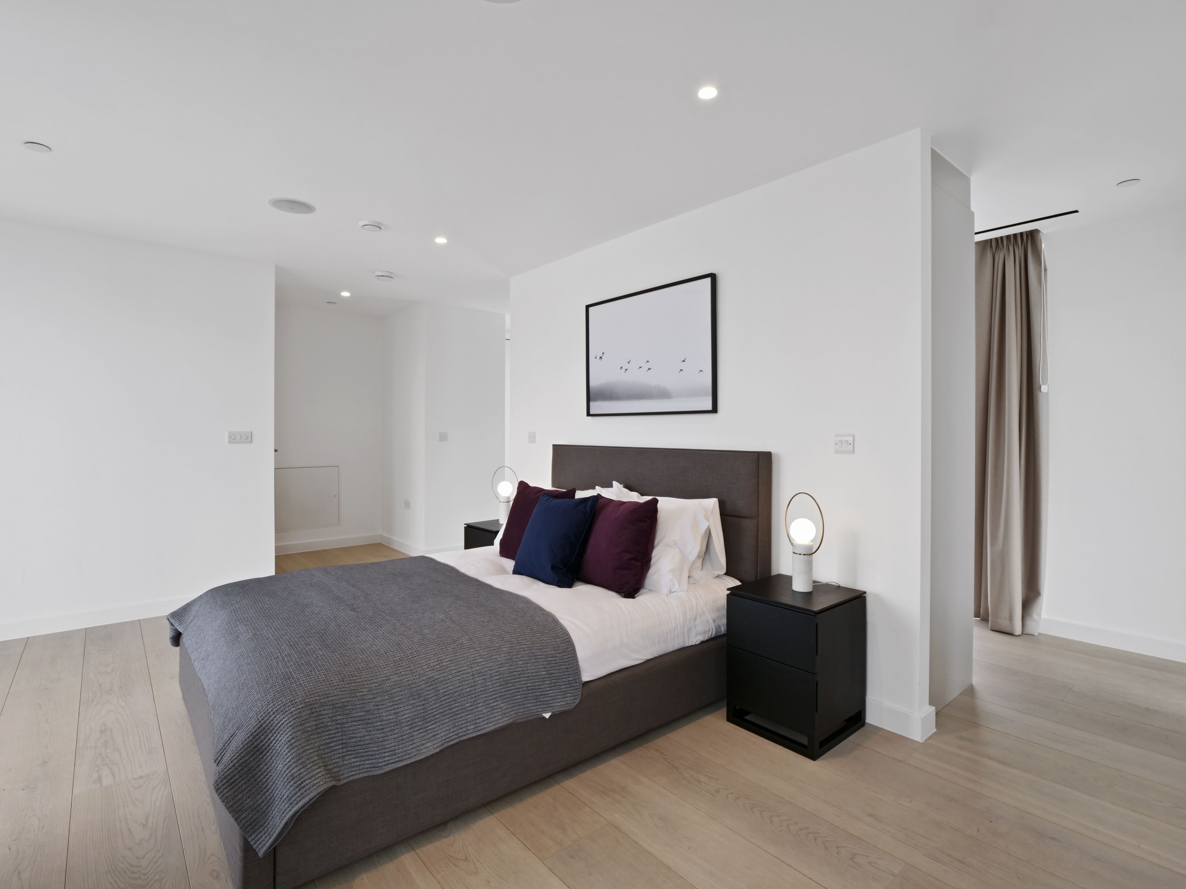 Un dormitorio moderno con una cama grande, mesitas de noche, un cuadro enmarcado en la pared y una ventana con cortinas.