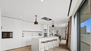 Une cuisine moderne avec des meubles blancs, un îlot central doté de tabourets et un éclairage suspendu.