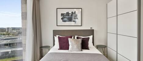 A modern bedroom with a large bed, a city view, and a contemporary light fixture.