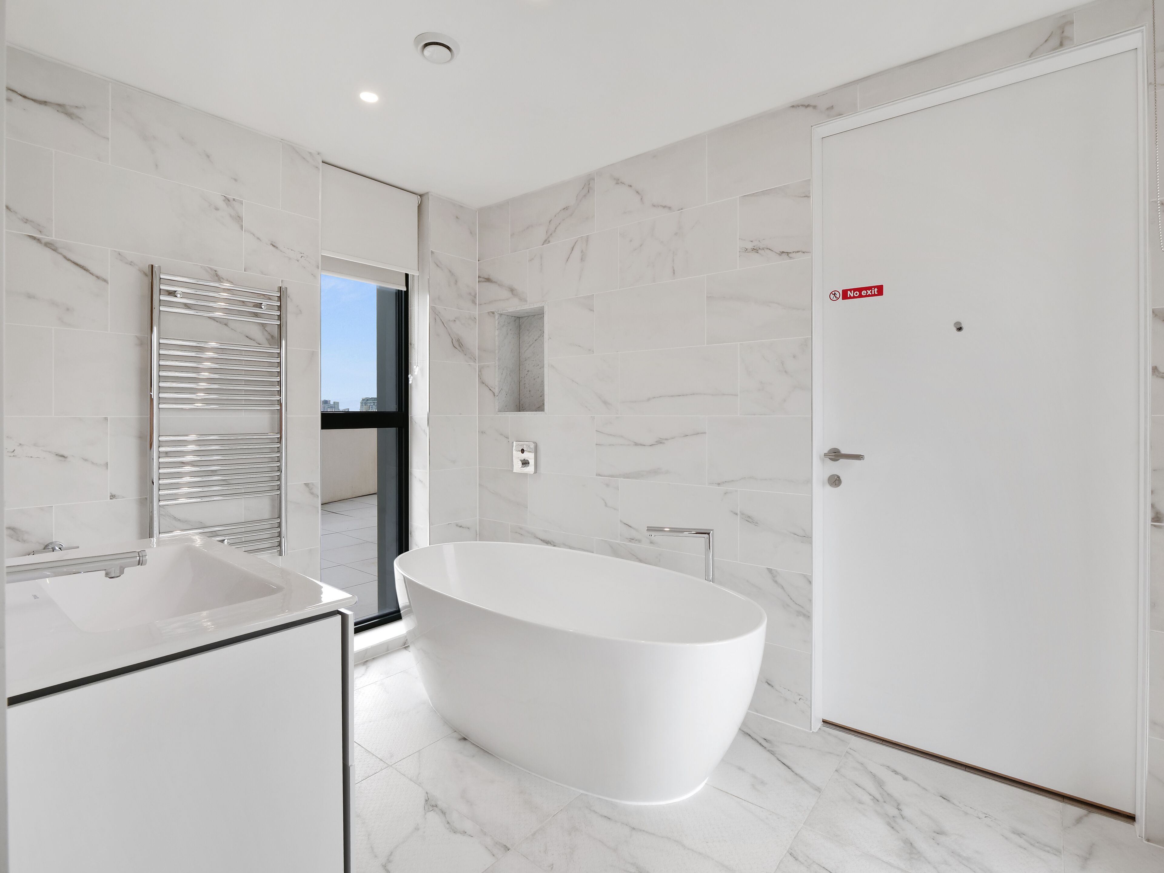 Ein modernes Badezimmer mit einer freistehenden Badewanne, einem großen Spiegel und einer weißen Tür mit einem „Kein Ausgang“ Schild.