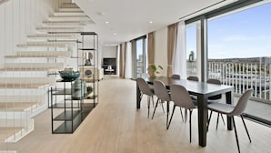 Un intérieur moderne comprenant un coin repas, un escalier et de grandes fenêtres offrant une vue sur la ville.