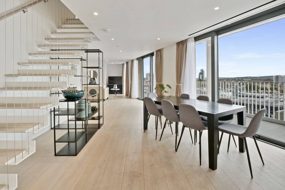 A modern interior with a dining area, staircase, and large windows offering a city view.