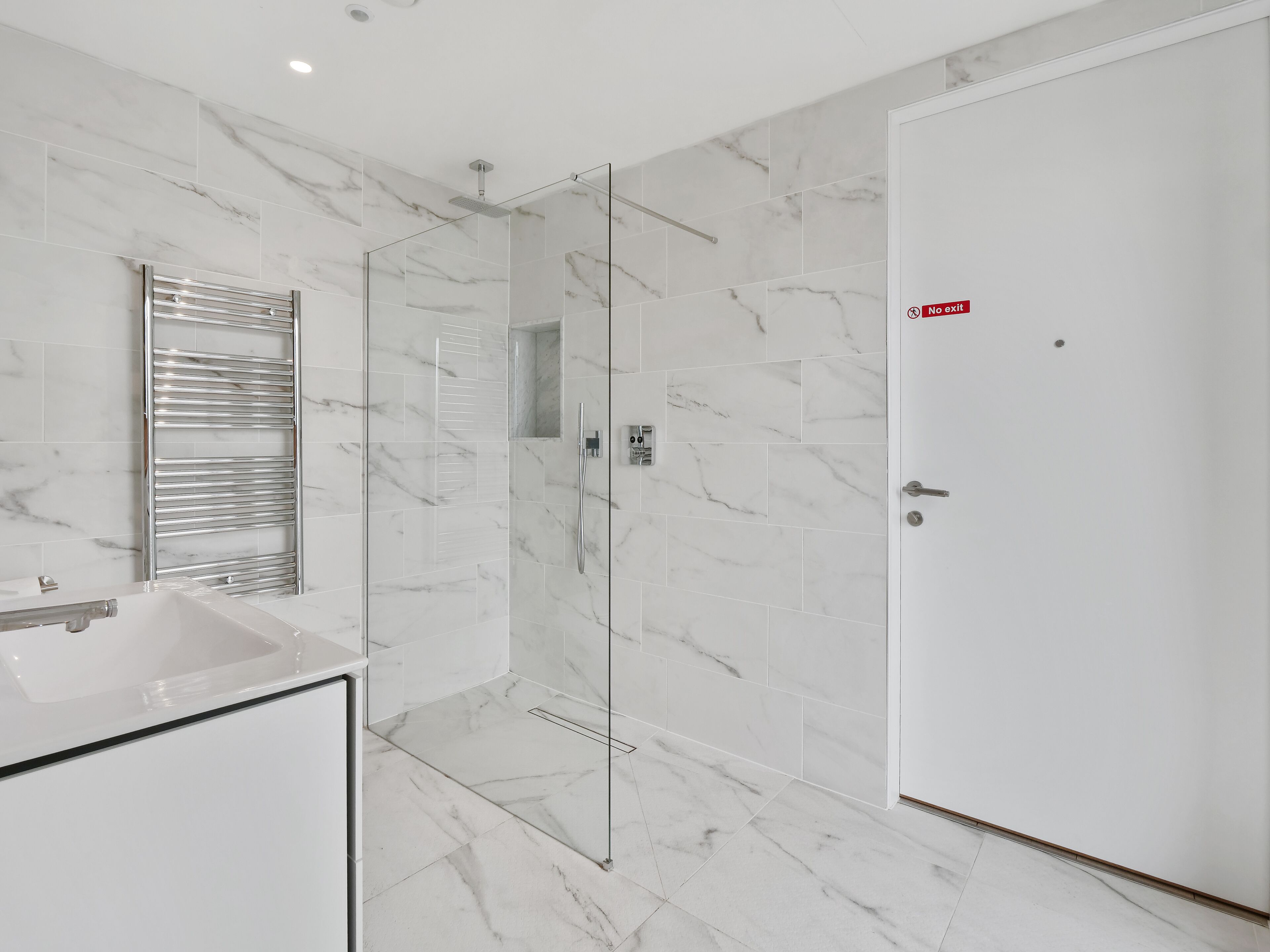 A modern bathroom with a glass shower enclosure, a white sink, and a door with a 'No Exit' sign.