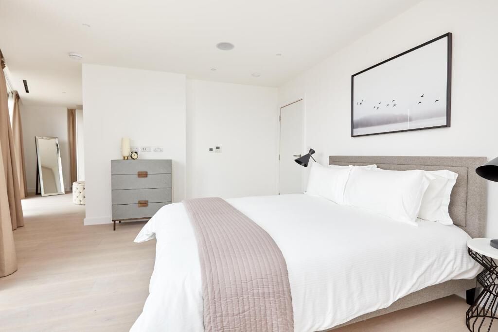 Un dormitorio moderno con una cama grande, un aparador, una mesita de noche y un cuadro enmarcado en la pared.