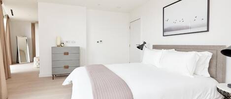 Un dormitorio moderno con una cama grande, un aparador, una mesita de noche y un cuadro enmarcado en la pared.