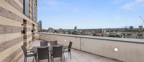 A rooftop terrace with a city view, featuring a table and chairs, and a sofa.