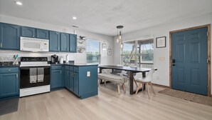 Een moderne keuken met blauwe kastjes, een witte magnetron en een eethoek met een bank en stoelen.