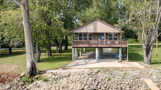 Een chalet met terras, omringd door bomen en een waterpartij.