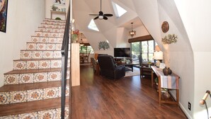 Een ruime loft met een houten trap, een plafondventilator en een eethoek met een televisie.