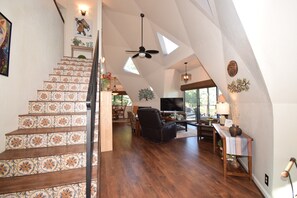 Ein geräumiges Loft mit einer Holztreppe, einem Deckenventilator und einer Essecke mit Fernseher.