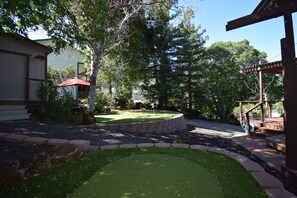 A backyard with a putting green, a wooden deck, and a covered seating area. - Tranquil Lake View Dome Home in Wine Country (Lower Lake)