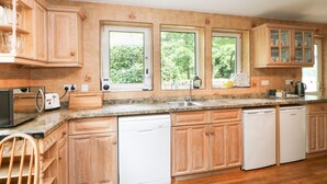 A kitchen with wooden cabinets, a dishwasher, a toaster, and a window with a view of greenery. - Bridgedown House (Richmond)
