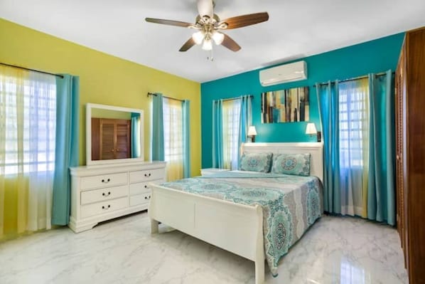 Quarto com cama, ventoinha no teto, penteadeira e janela com cortinas.