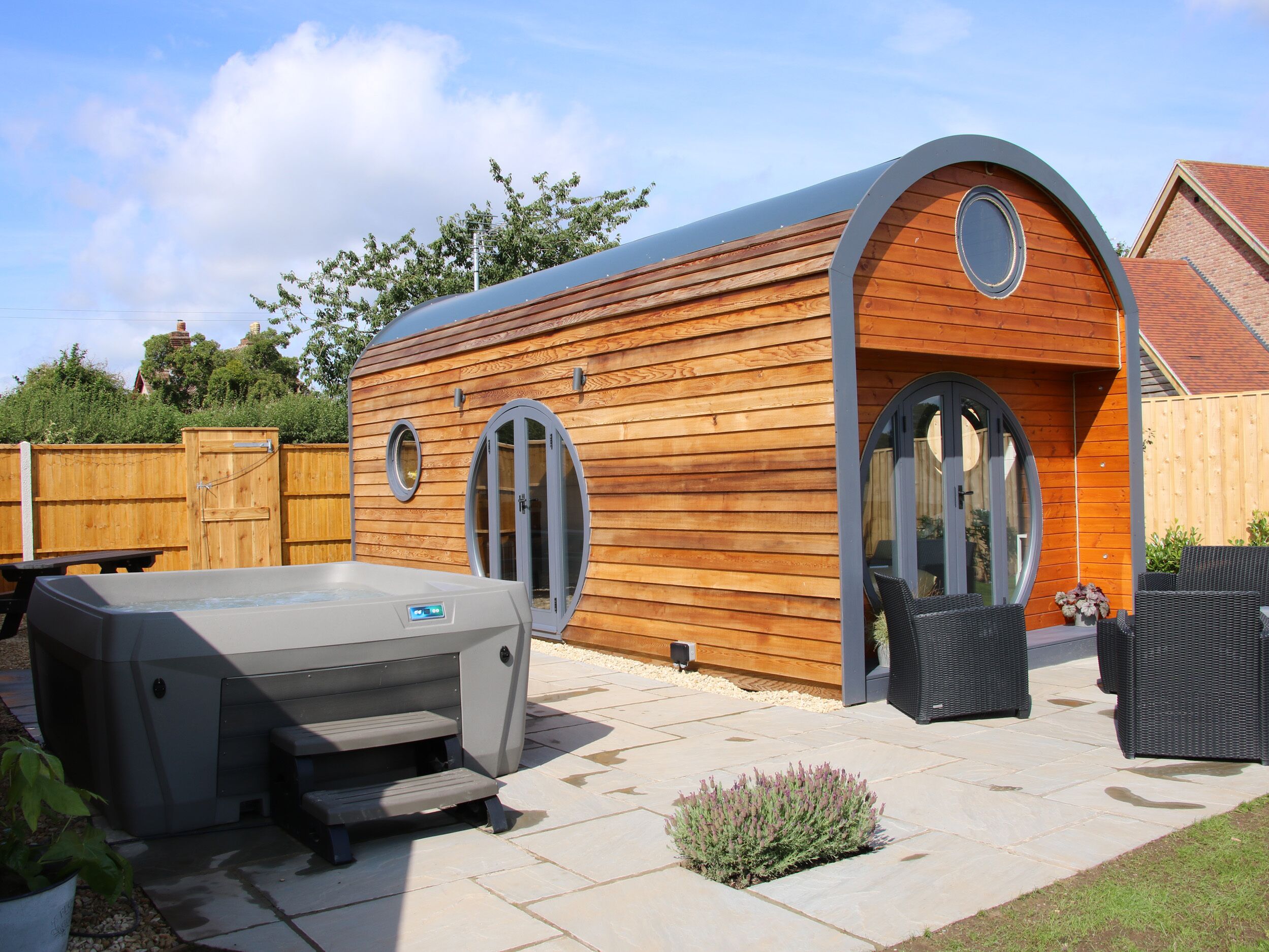 Une cabane en bois dotée d’un toit incurvé, d’un bain à remous et d’un espace salon extérieur.