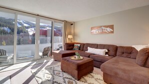 A living room with a brown sofa set, a glass sliding door to a balcony, and a mountain view.
