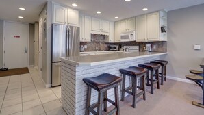 A modern kitchen with white cabinets, stainless steel appliances, and a bar area with stools.