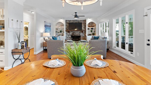 Amplia sala de estar con chimenea, comedor con mesa de madera y ventanas grandes con vistas al exterior.
