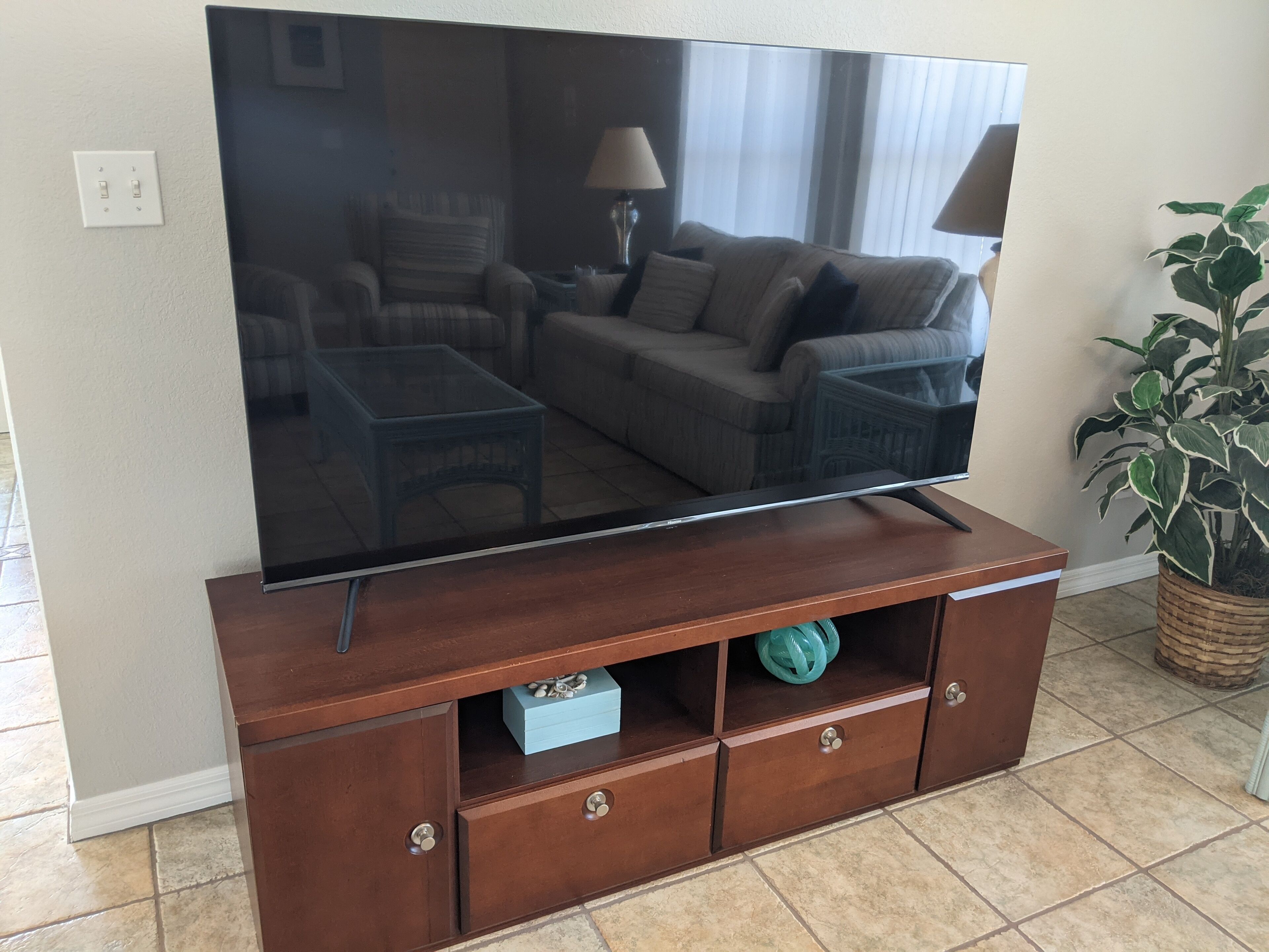 Un televisor de pantalla plana sobre un mueble de madera con cajones y un estante, una planta en maceta y una lámpara.