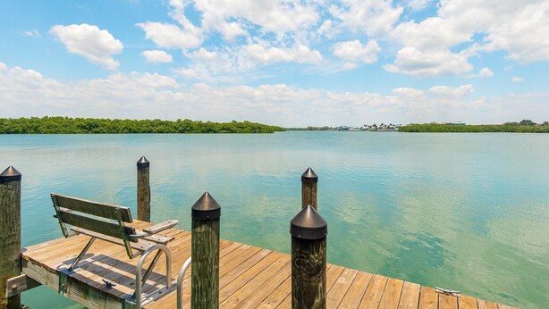 A wooden dock with a bench and metal bollards, leading to calm turquoise waters.