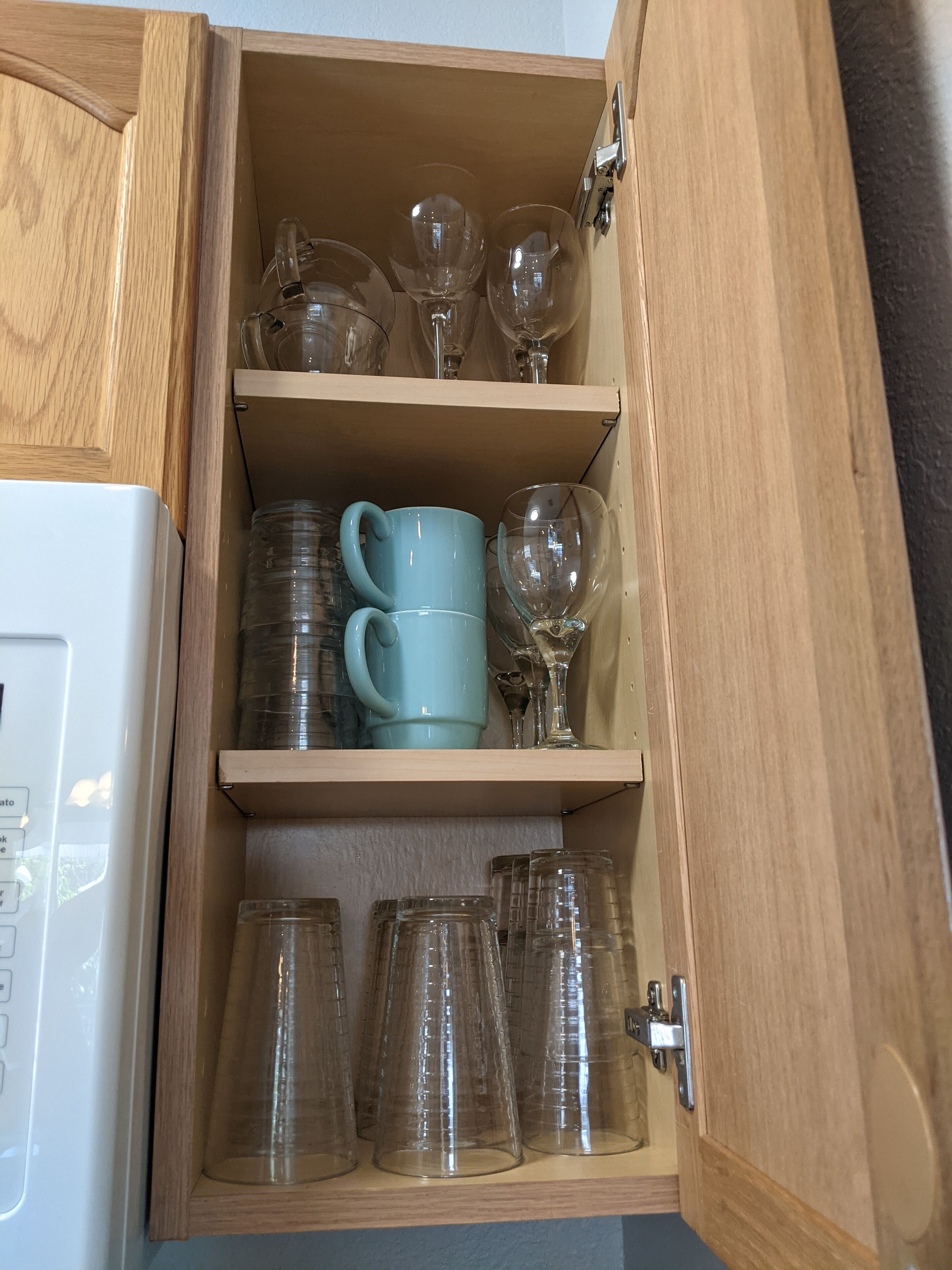 A wooden cabinet with shelves containing various glassware, including wine glasses and clear mugs.