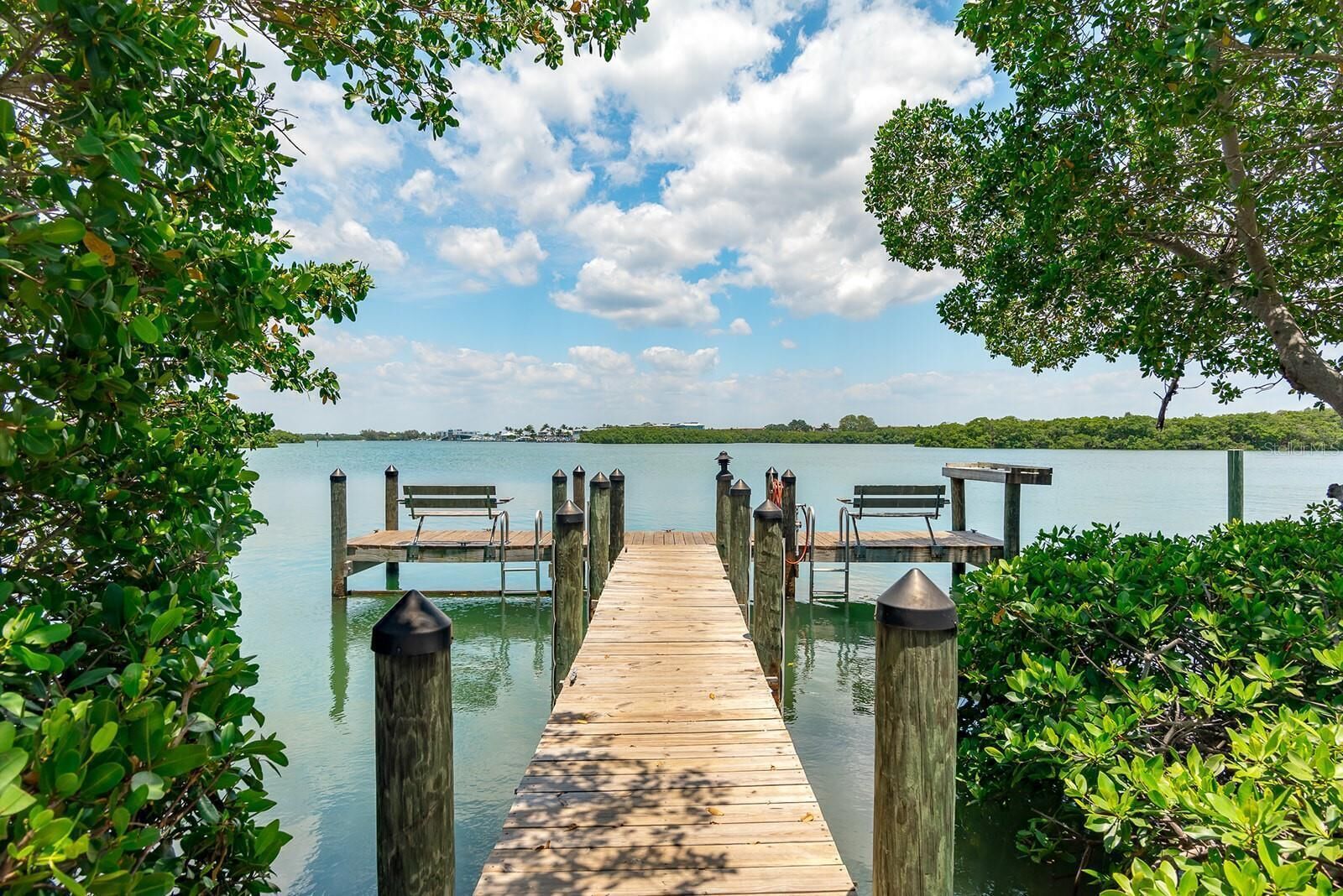Eine hölzerne Pier, die zu einem Steg mit Bänken führt, umgeben von üppigem Grün und einem ruhigen See.