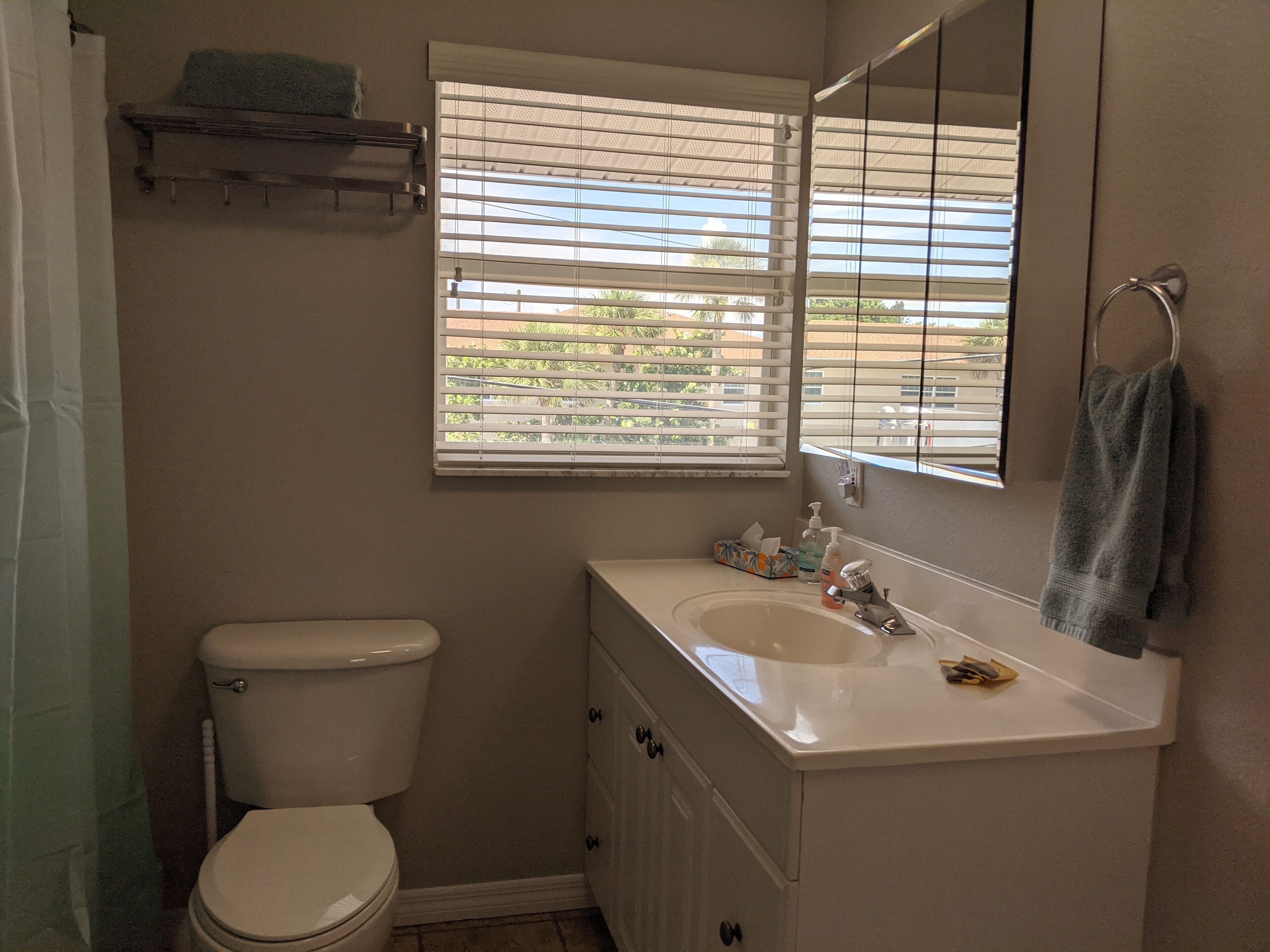 Une salle de bain avec des toilettes, un lavabo et une fenêtre équipée de stores.