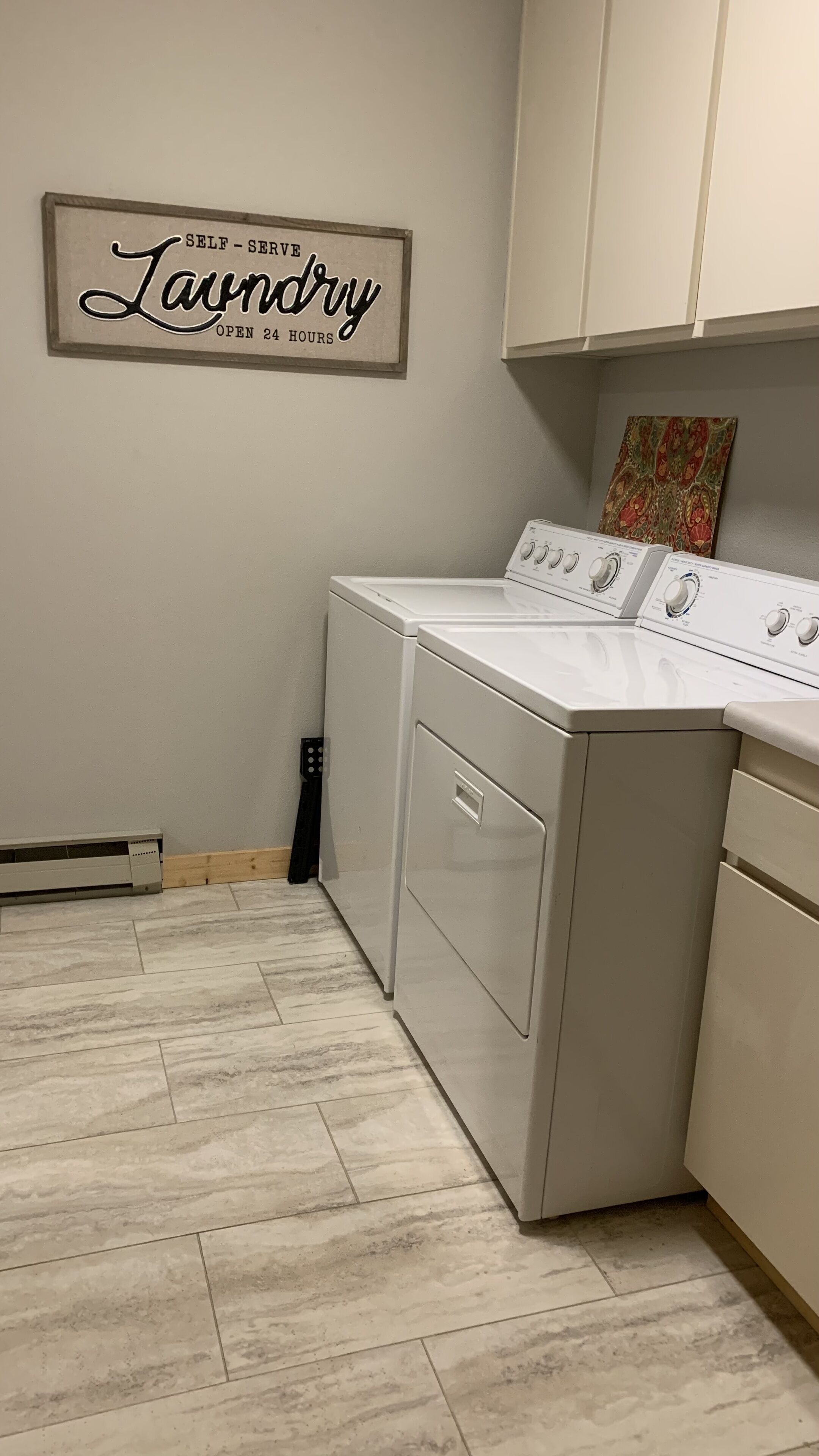 A laundry room with a sign that reads 'SELF-Serve Laundry OPEN 24 HOURS.'