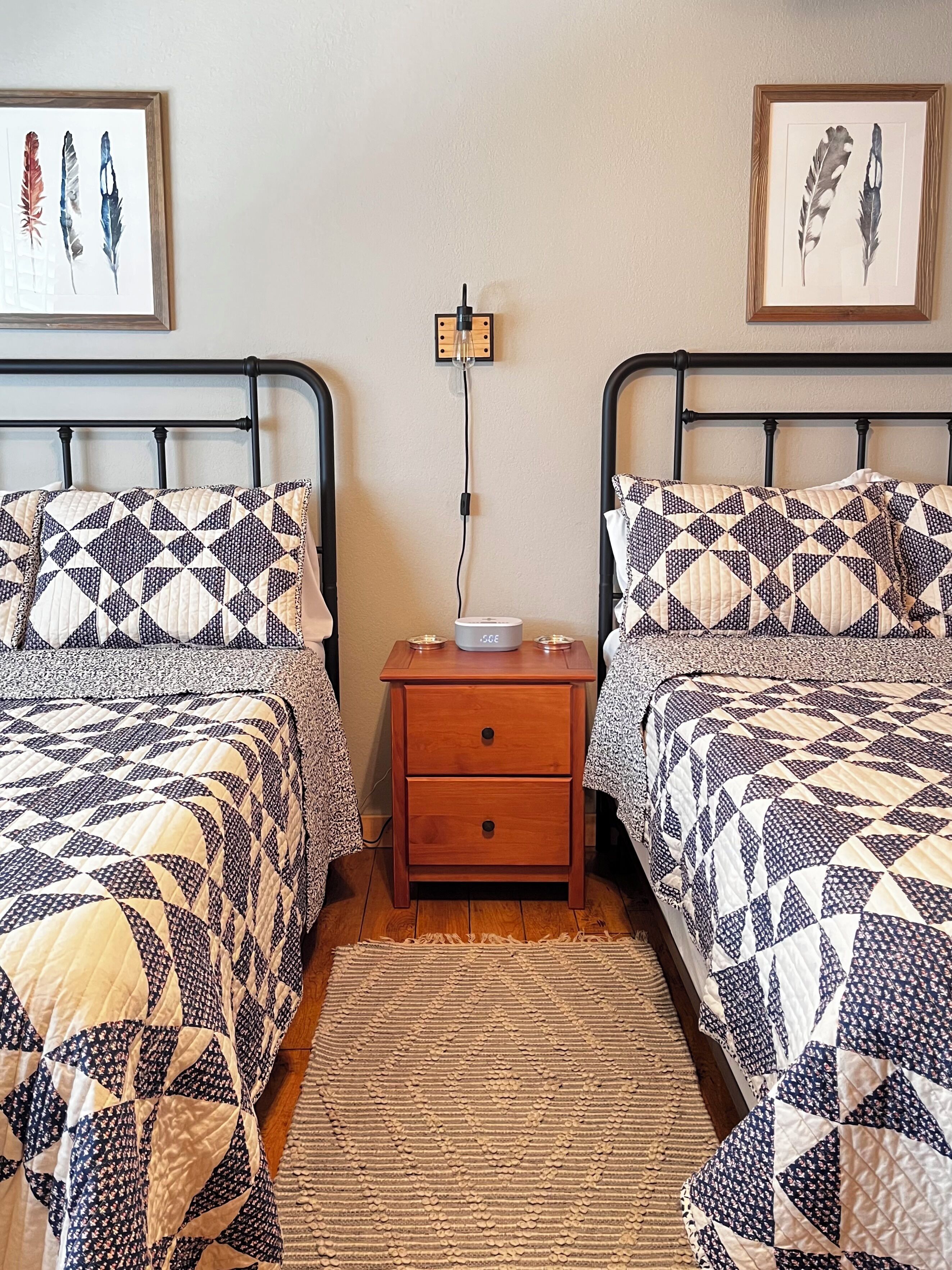 A bedroom with two beds, a nightstand with a lamp, and framed artwork on the wall.