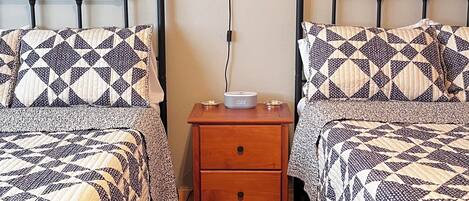 A bedroom with two beds, a nightstand with a lamp, and framed artwork on the wall.