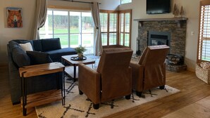 A cozy living room with a dark sofa, two brown armchairs, a wooden coffee table, and a stone fireplace. - Cozy Condo on the 4th Fairway of  Plumas Pines Golf Course (Blairsden Graeagle)