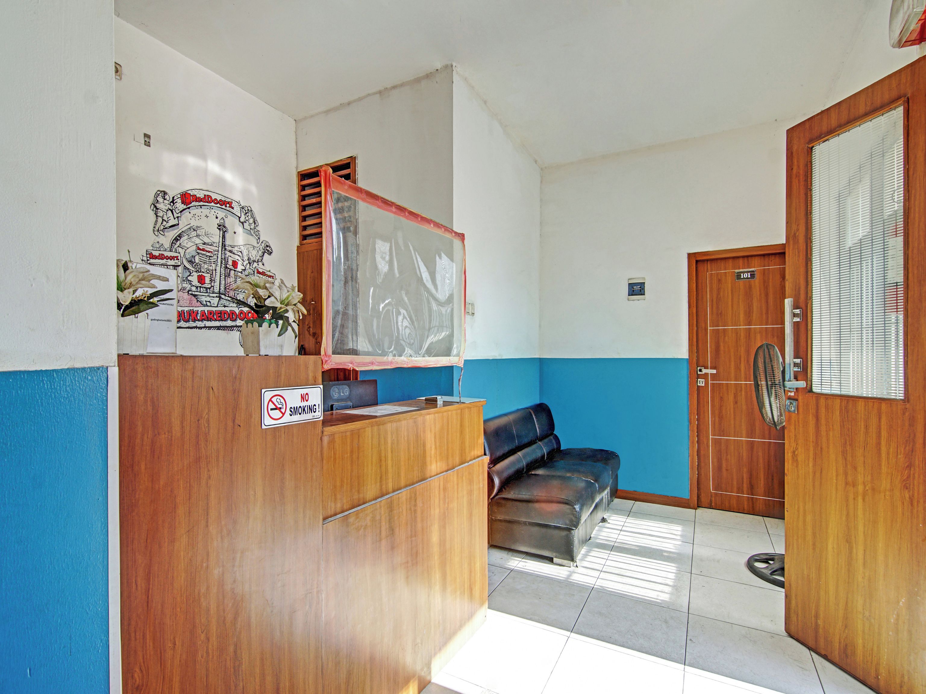A reception area with a wooden desk, a blue wall, a black leather couch, and a door marked "101".