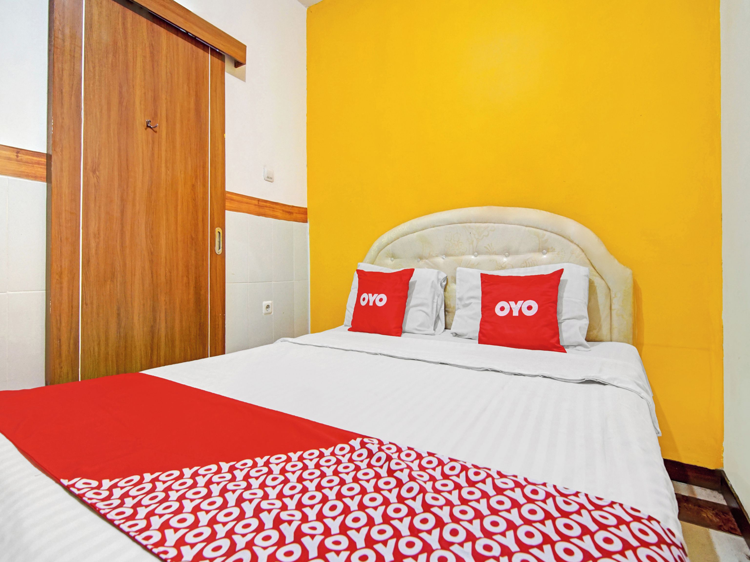A hotel room with a bed, a wooden door, and a yellow wall.